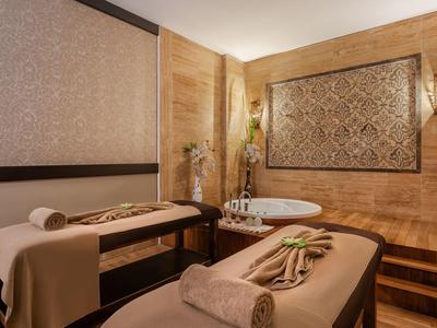 Sala spa di lusso con due lettini per massaggi, vasca da bagno e accenti caldi in legno.