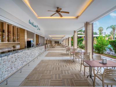 Area esterna coperta dell'hotel con bar, tavoli e vista su giardini tropicali.