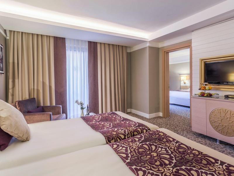 Camera d'hotel moderna con due letti, TV a schermo piatto e angolo salotto accogliente.