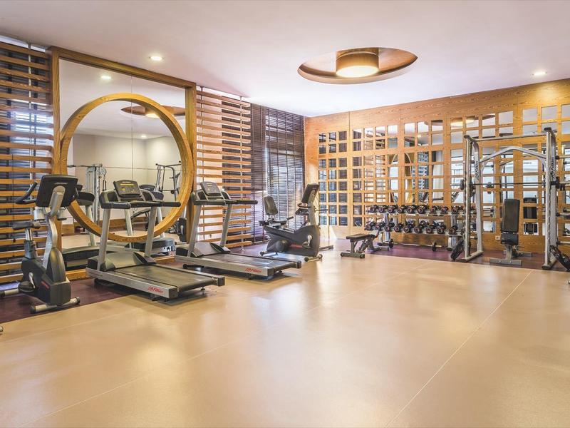 Palestra luminosa con varie attrezzature, parete a specchio e dettagli in legno.