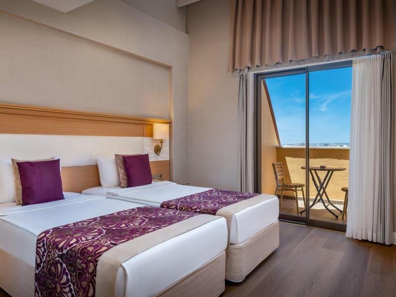 Camera d'hotel moderna con letto matrimoniale, decorazioni viola e balcone con vista mare.