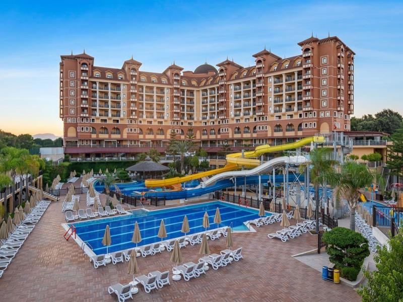 Grande hotel a più piani con piscina all'aperto e lettini sotto un cielo sereno.