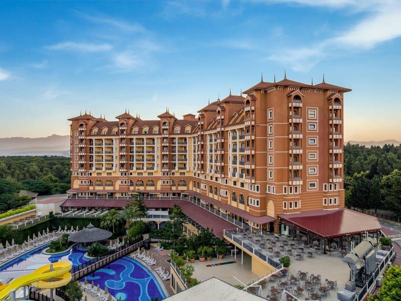 Grande hotel multipiano con giardino, piscina e scivolo d'acqua davanti a uno sfondo boscoso.