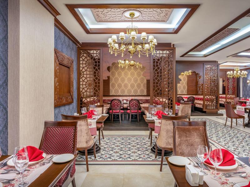 Ristorante elegante con lampadario, pareti decorate e tavoli apparecchiati con tovaglioli rossi.