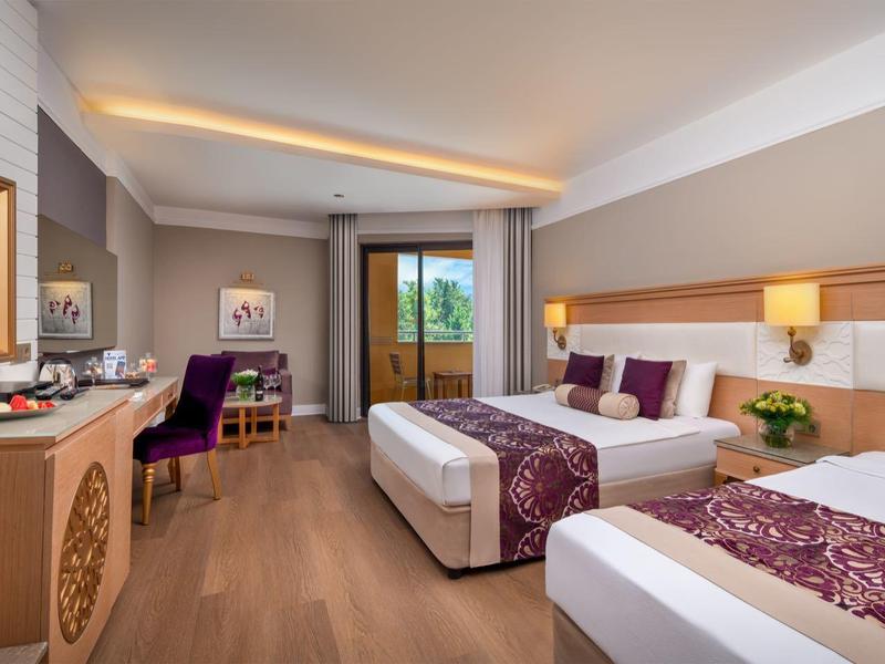 Camera d'hotel moderna con due letti, scrivania, TV a schermo piatto e balcone con vista sulla natura.