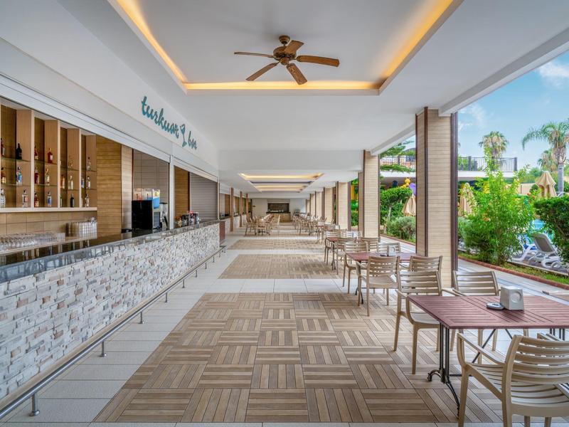 Area esterna coperta dell'hotel con bar, tavoli e vista su giardini tropicali.