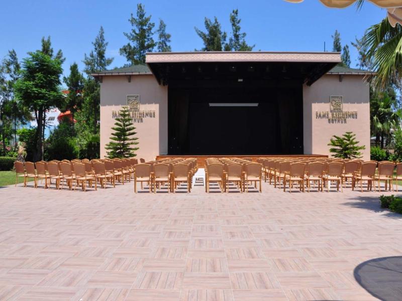 Palco all'aperto con file di sedie e alberi sullo sfondo in una giornata di sole