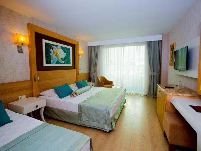 Camera d'hotel luminosa con due letti, scrivania, sedia e finestra con tende.