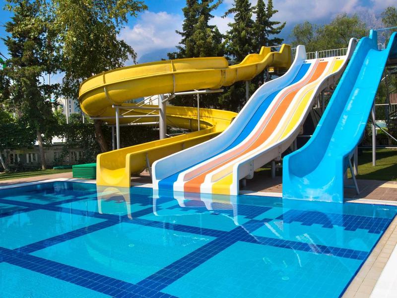 Diverse scivoli d'acqua colorati terminano in una piscina limpida circondata da verde.