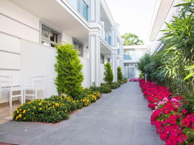 Moderner Hausgang mit weißen Wänden, grauem Boden, grünen Pflanzen und bunten Blumen an beiden Seiten.