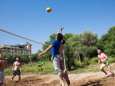 Quattro uomini giocano a beach volley su un campo sabbioso all'aperto sotto un cielo sereno.