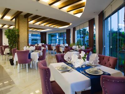 Elegantes Restaurant mit violetten Stühlen, weißen Tischdecken und großen Fenstern, Tageslicht fällt herein.