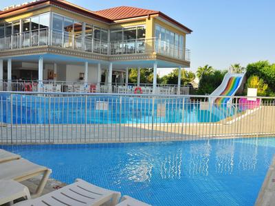 Großer Außenpool mit Wasserrutschen vor einem zweistöckigen Gebäude mit roten Dächern und Glaswänden.
