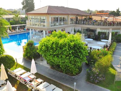 Modernes Gebäude mit glasumrahmtem Poolbereich, umgeben von grünen Pflanzen und Sonnenliegen.