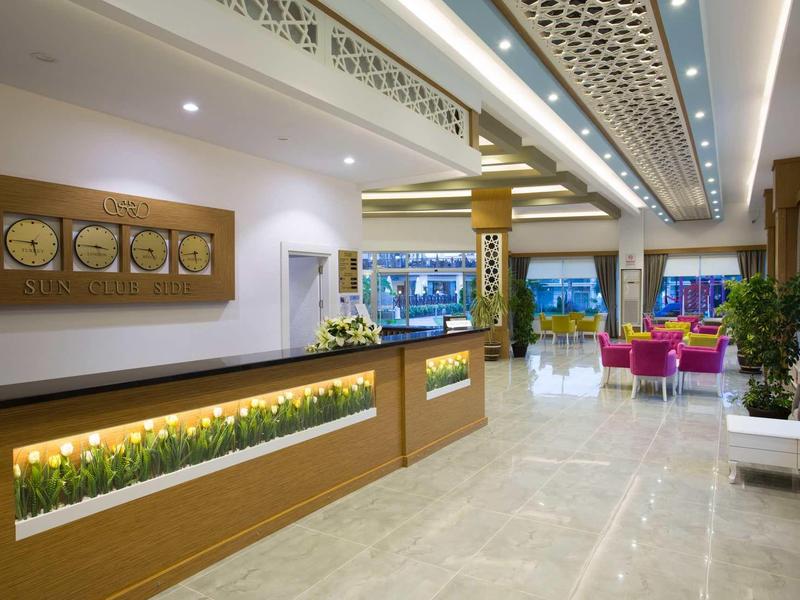 Innenraum einer modernen Hotellobby mit Rezeptionstresen, Pflanzen und Sitzbereichen in hellem Design.