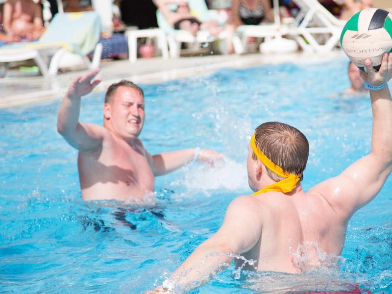 Zwei Männer spielen Wasserball im Pool, einer hält den Ball, der andere ist im Wasser.