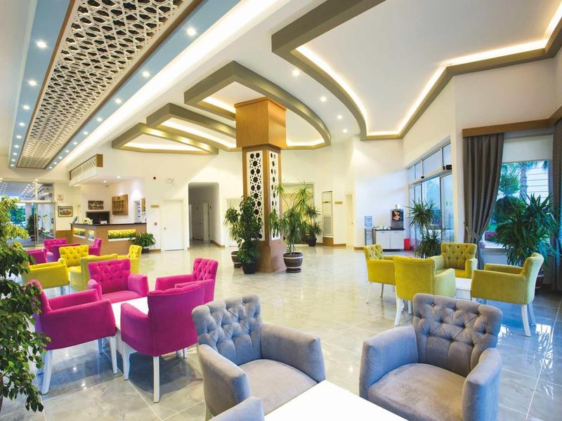 Heller, moderner Wartebereich mit bunten Sesseln, Pflanzen und einem dekorativen Deckenlicht.