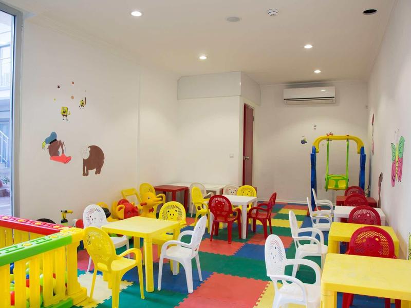 Kinderzimmer mit bunten Tischen, Stühlen, Spielzeug und weichem Bodenbelag in hellem Raum.