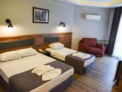 Hotelzimmer mit Doppel- und Einzelbett, braunen Holzmöbeln, Sessel und Klimaanlage.