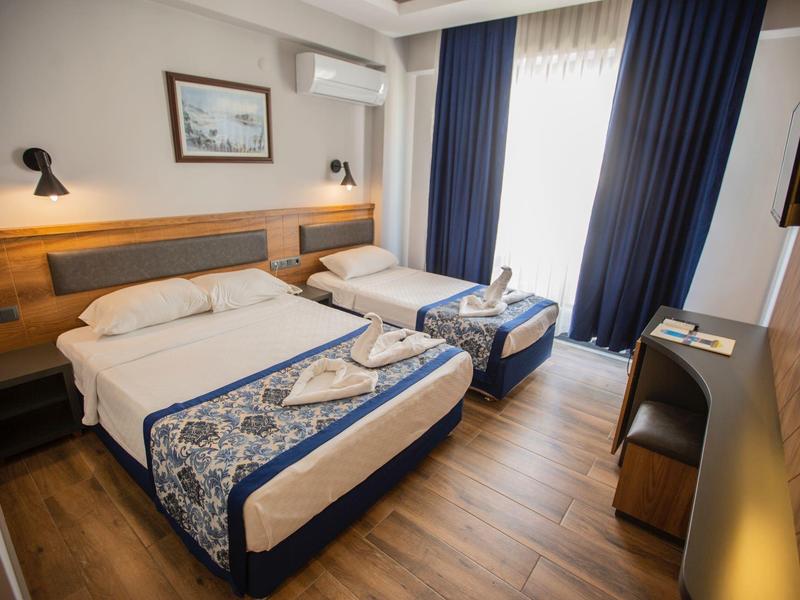 Modern hotelkamer met tweepersoonsbed, eenpersoonsbed, balkon, houten vloer en blauwe gordijnen.