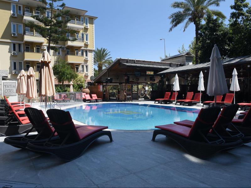Rond zwembad met rode ligstoelen en parasols naast een hotelgebouw.