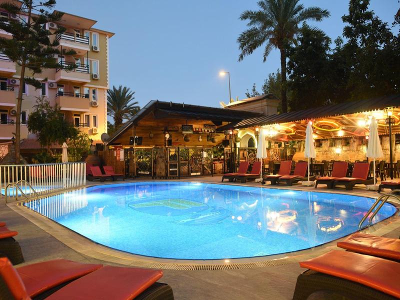 Verlicht hotelzwembad met ligbedden en overdekt terras in de avond