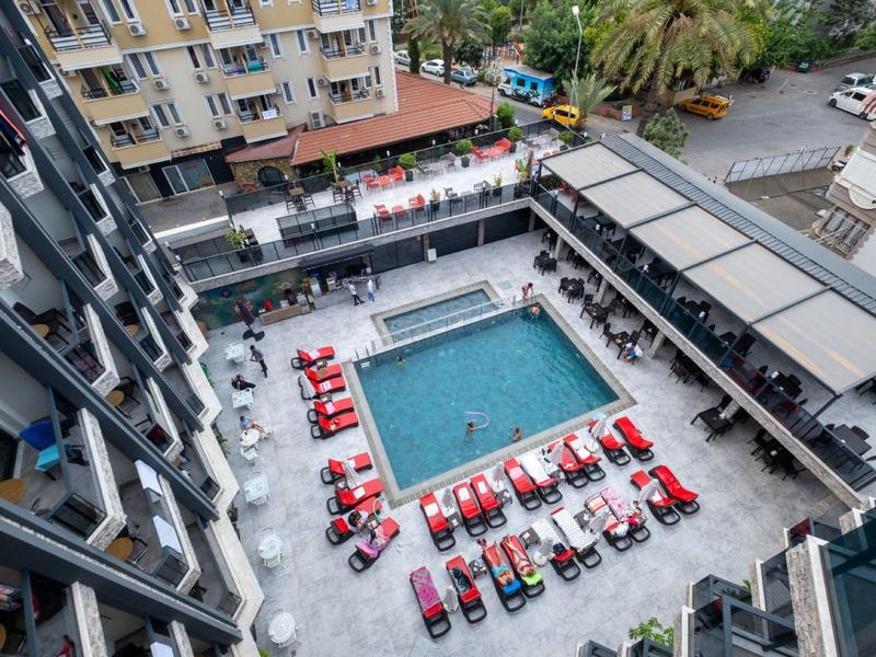 Bovenaanzicht van een hotelzwembad met rode ligbedden en omliggende gebouwen.