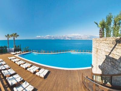 Infinity-Pool mit Holzdeck, Liegestühlen und Palmen, Blick auf das blaue Meer und klare Himmel.