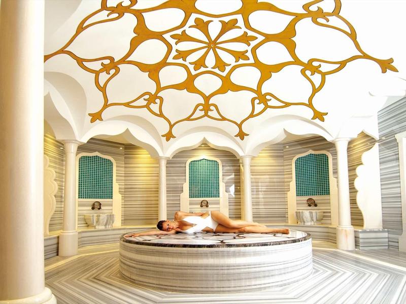 Lichte, sierlijke hammam sauna met gouden plafond en ronde marmeren bank in het midden.