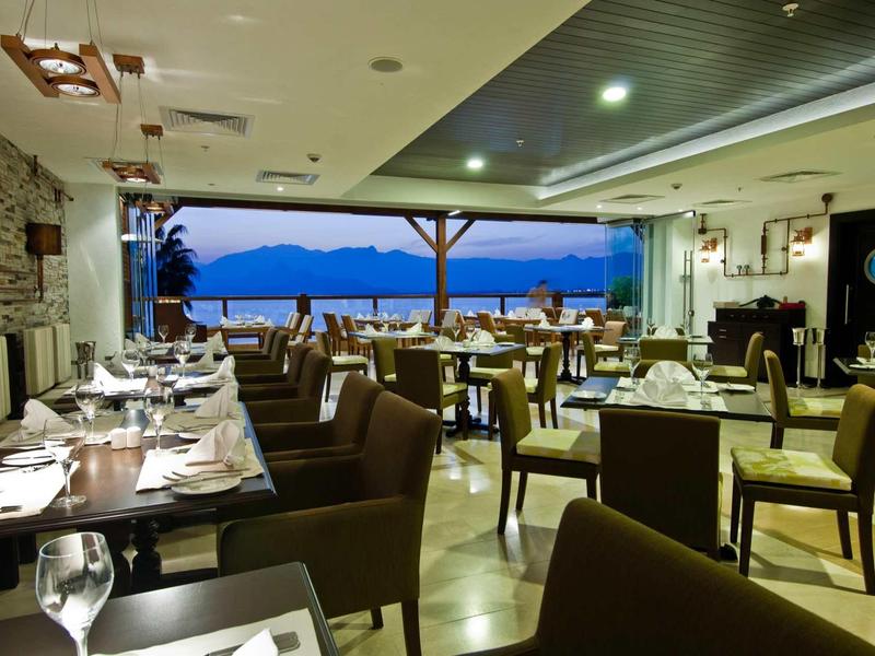 Elegante hotelrestaurant met zitgedeeltes, verlichte tafels en uitzicht op bergen bij schemering.