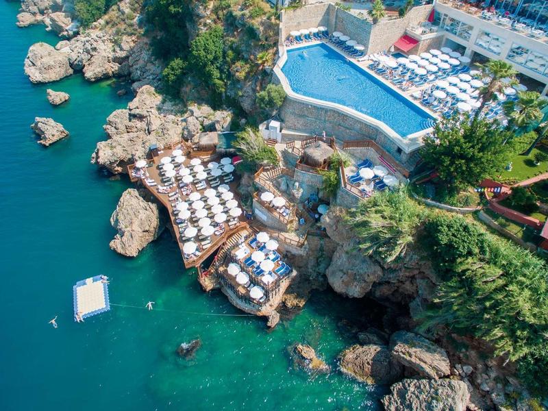 Kusthotel met zwembad en meerdere terrassen boven de zee met parasols en ligstoelen.