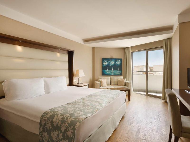 Lichte hotelkamer met groot bed, zithoek en balkon met uitzicht naar buiten.