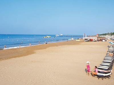 Ampie spiagge sabbiose tranquille con file di sedie a sdraio e mare calmo sullo sfondo.