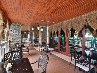 Terrazza esterna coperta con tetto in legno, colonne di pietra e tavoli e sedie decorative.