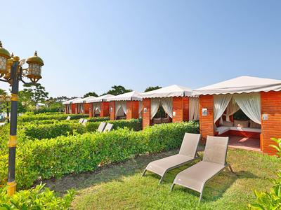 Giardino dell'hotel con lettini, siepi verdi e un'area lounge coperta sotto un cielo azzurro.