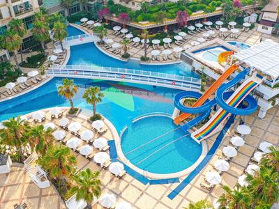 Großer Hotelpool mit mehreren Wasserrutschen, vielen Sonnenliegen und Palmen, umgeben von Gebäuden.