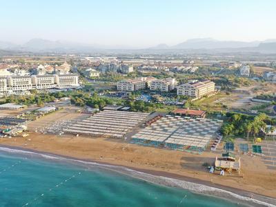 Vista aerea di un hotel su una spiaggia sabbiosa con piscine e paesaggio circostante.