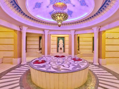 Sala spa circolare luminosa con bacino in marmo, petali rosa e decorazioni tradizionali.