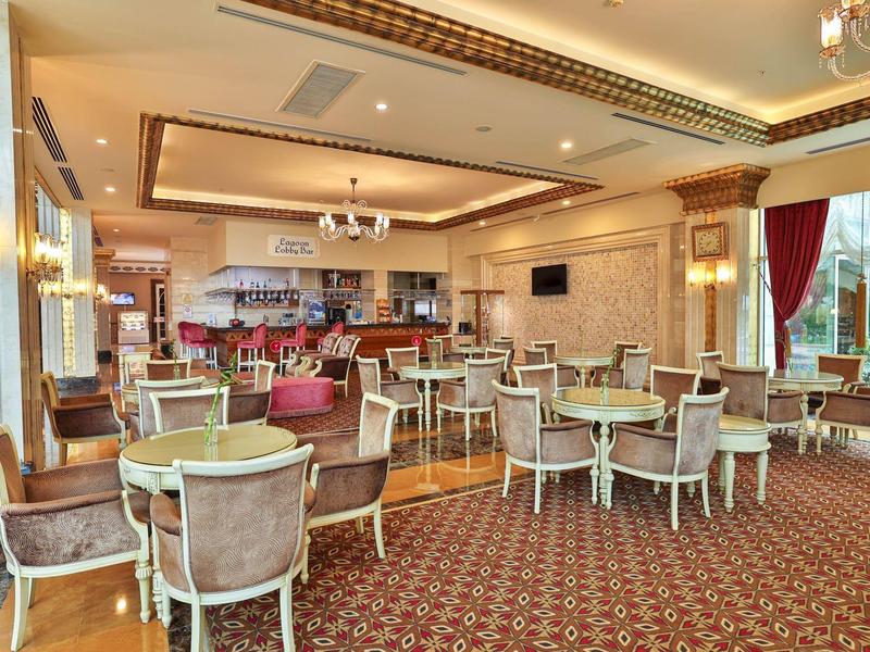 Sala da pranzo elegante dell'hotel con mobili in legno, moquette, illuminazione luminosa e vista dalle finestre.