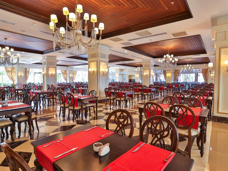 Grande sala da pranzo elegante con mobili in legno, tovagliette rosse e lampadari.