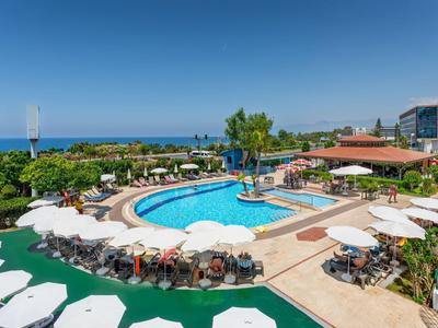 Hotelpool mit Sonnenschirmen, Liegen und Meerblick unter klarem Himmel.