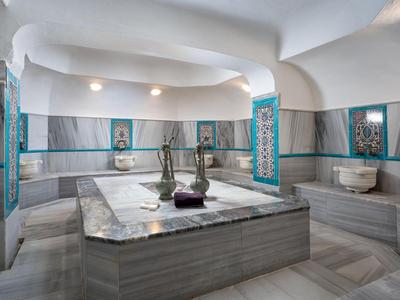 Heller türkischer Hamam mit Marmorliegen, geschwungenen Decken und zentralen Wassergefäßen.