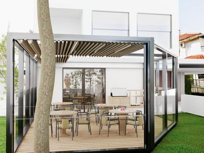 Moderner Glasraum mit Holzveranda und Metallmöbeln auf grünem Rasen neben einem Baum.
