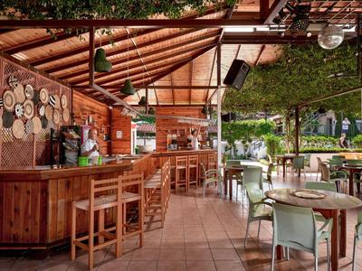 Offene Bar mit Holzmöbeln und grüner Dachbegrünung in einem Hotelgarten.