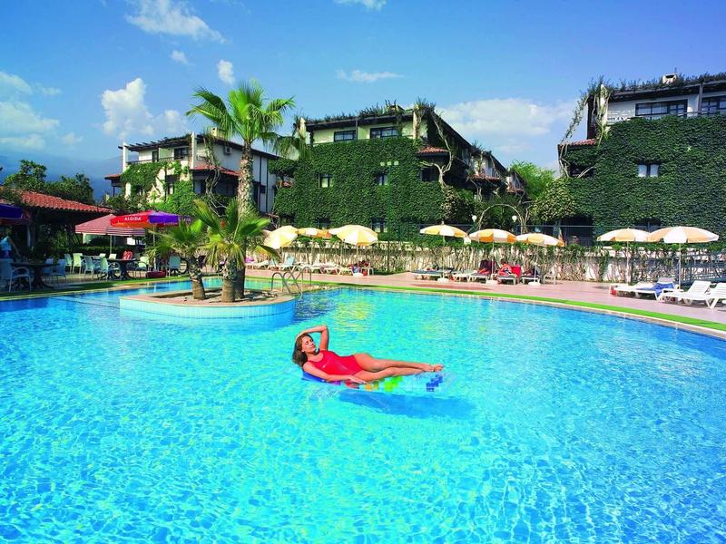 Personne flottant dans une grande piscine claire près d'un hôtel verdoyant.