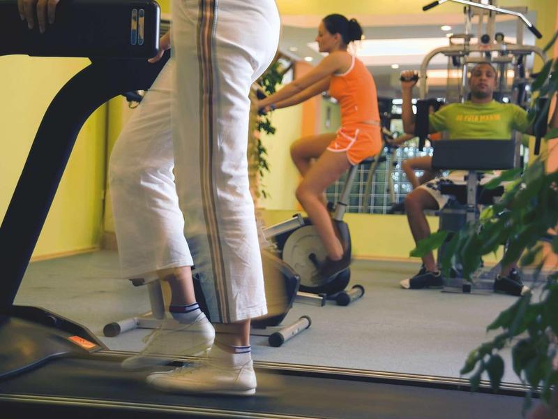 Trois personnes font de l'exercice dans une salle de sport lumineuse avec tapis roulants et vélos.