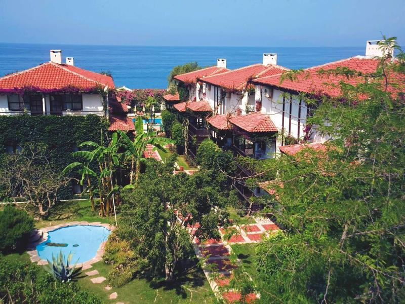 Hôtel avec jardins luxuriants et piscine, vue sur la mer au loin.