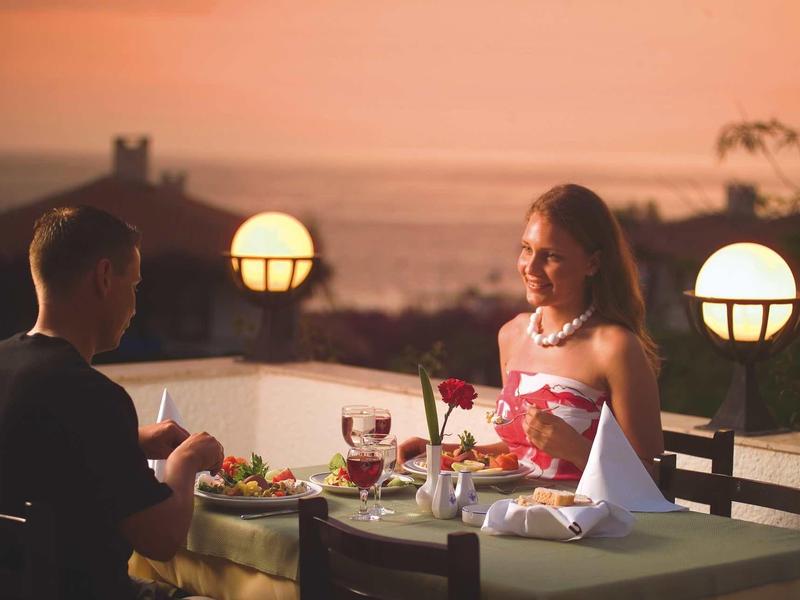 Un couple dîne en terrasse au coucher du soleil avec vue sur la mer.
