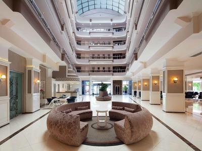 Helles, modernes Atrium mit runden Sitzgruppen, Glasdach und mehreren Etagen mit weißen Wänden.