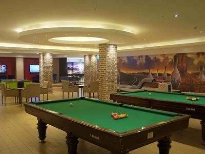 Game room with pool tables, seating areas, and modern lighting in a hotel.
